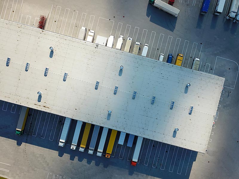 Aerial perspective of a spacious warehouse with multiple trucks positioned around it, indicating active shipping activities.