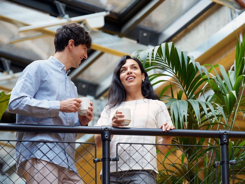 Deux personnes en discussion avec un tasse à la main et des plantes vertes dans le fond