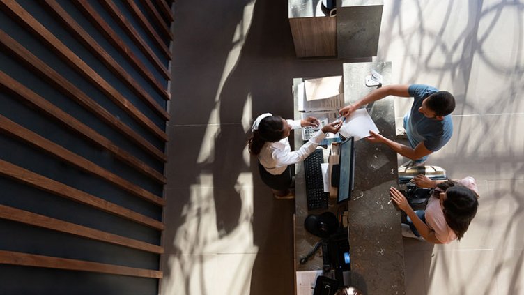 a male and female at hotel reciption taking a form from receptionist to fill in