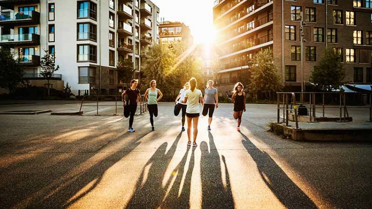 A fitness instructor talking to her class outdoors in the city.