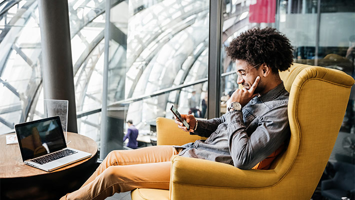 A business owner sitting in a comfortable chair in a modern office space, using his smartphone.