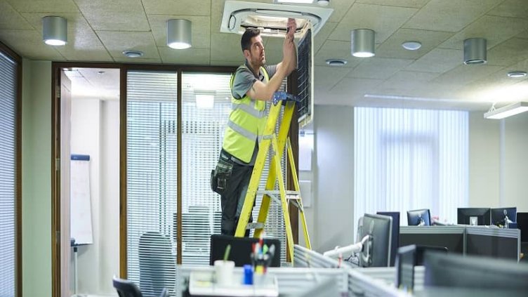 A man is fixing the light on the workspace inside the office