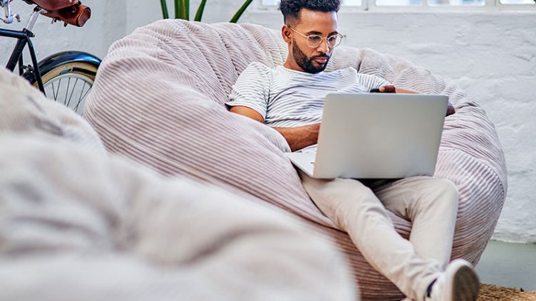 Man sat on cushion, working on his laptop.