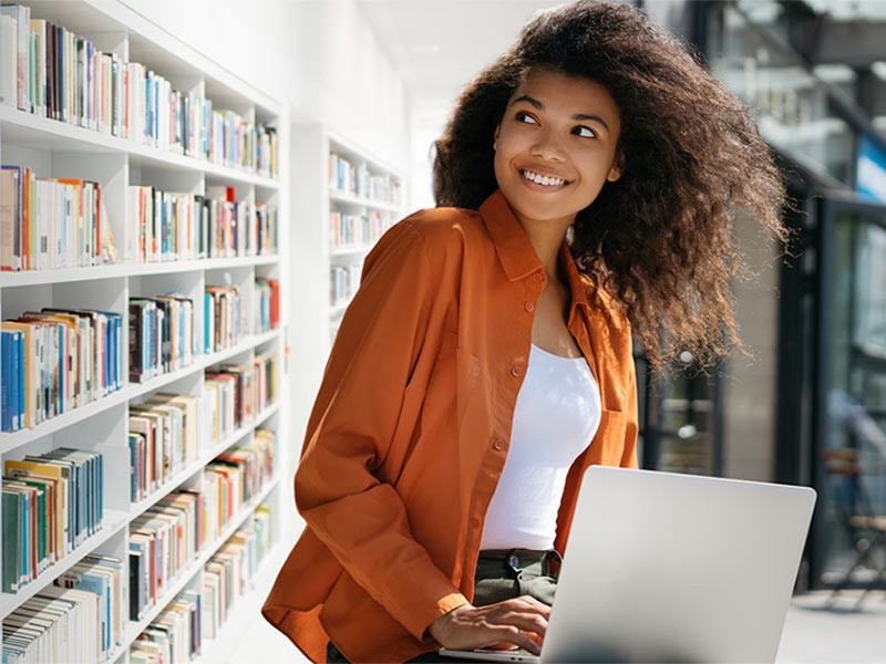 Young girl working on a computer with a shelf of books behind her